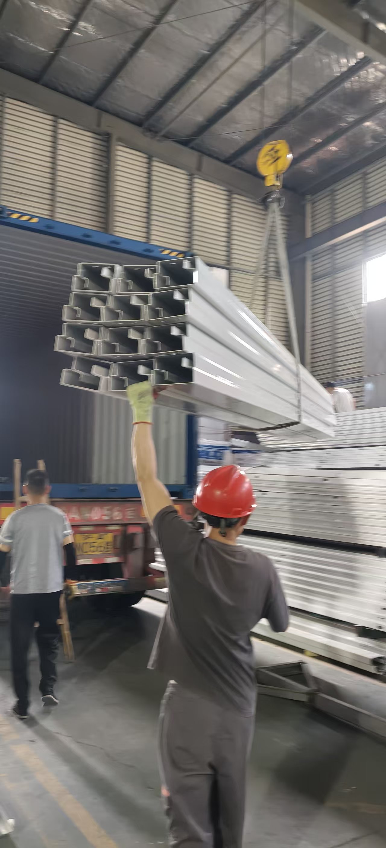 Worker in red helmet lifting metal beams with crane in warehouse